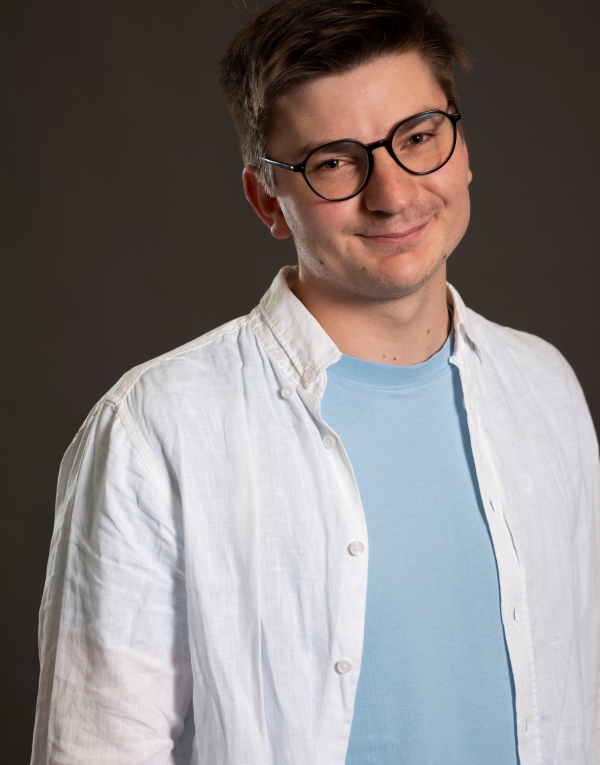 Oberkörper eines Mannes mit hellblauem T-Shirt und weißem Hemd vor dunklem Hintergrund