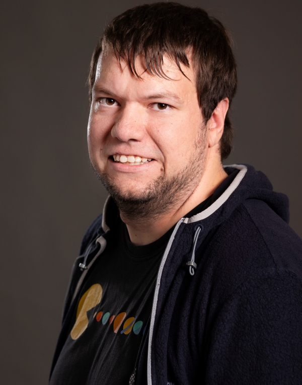 Mann mit dunklem Kapuzenpullover und T-Shirt mit farbigem Muster vor dunklem Hintergrund