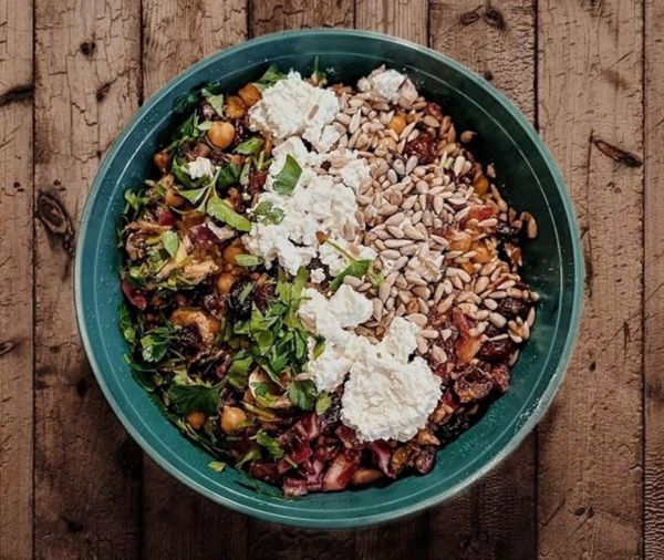 Grüner Teller mit einer Mischung aus Kichererbsen, gehackter Petersilie, Sonnenblumenkernen und mehreren Klecksen weißem Frischkäse auf Holztisch