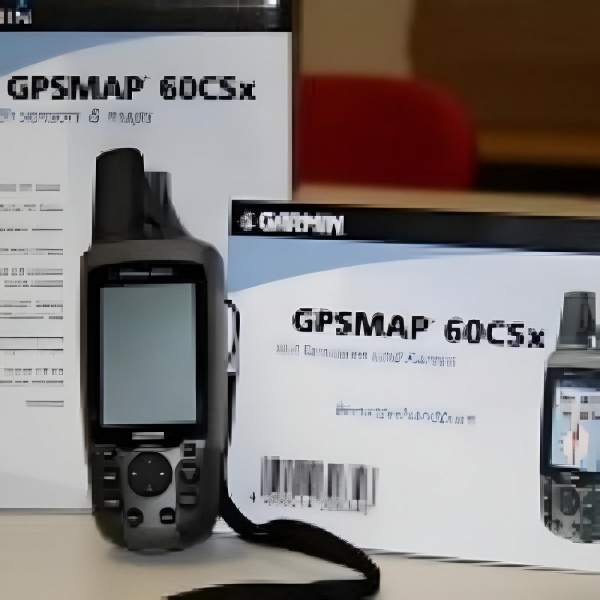 Im Vordergrund steht ein tragbares GPS-Gerät mit großem Display, mehreren Tasten und einer Antenne. Das Gerät ist dunkelgrau und hat eine Handschlaufe. Im Hintergrund sind zwei Produktverpackungen mit der Aufschrift 'GPSMAP 60CSx' zu sehen. Auf einer Verpackung ist ein Foto des Geräts abgebildet.